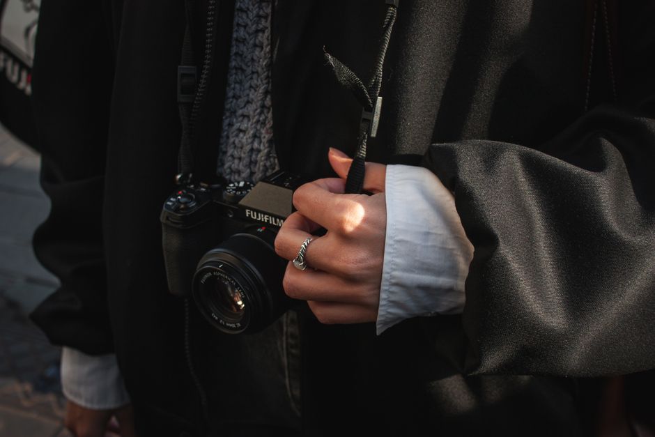 A person wearing a black coat holds a camera strap tightly. Street photography ambiance.